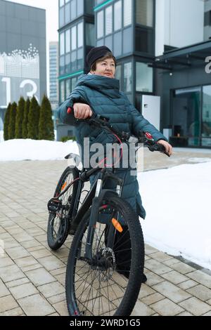 Reife Europäerin im Wintermantel fährt mit dem Fahrrad durch die Straßen der Stadt Stockfoto