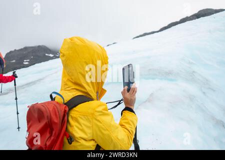 Frau, die Fotos des Gletschers mit dem Smartphone auf dem Exit Glacier macht. Nicht erkennbare Menschen, die im Hintergrund wandern. Kenai Fjords National Park. A Stockfoto