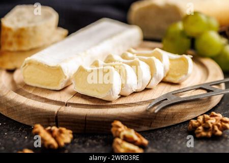 Handwerklicher Brie-Käse, geschnitten auf einem runden Holzschneidebrett, serviert mit Trauben und Walnüssen, ideales Bild für Gourmet-Käsekonzepte Stockfoto