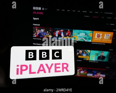 Person, die ein Smartphone mit dem Logo des britischen Video-on-Demand-Dienstes BBC iPlayer vor der Website hält. Schwerpunkt auf dem Display des Telefons. Stockfoto