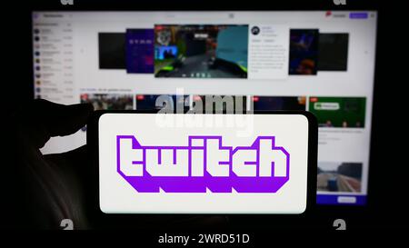 Person, die ein Mobiltelefon mit dem Logo des US-amerikanischen Live-Streaming-Unternehmens Twitch Interactive Inc. Vor der Webseite des Unternehmens hält. Schwerpunkt auf dem Display des Telefons. Stockfoto