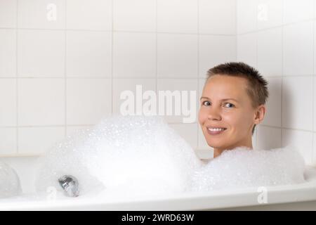 Dame mittleren Alters, die sich in einem luxuriösen Schaumbad verwöhnt Stockfoto