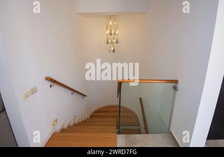 Blick auf eine geschwungene Holztreppe in einem modernen Luxushaus mit Kronleuchter und glasbannister Stockfoto