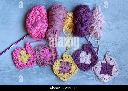 Handgemachtes Häkeln. Rosafarbene, lila, gelbe und weiße Granny-Quadrate. Niedliches Muster Nahaufnahme Foto. Weiche Baumwollgarnstruktur. Grauer Hintergrund mit Stockfoto