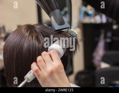 Die Friseurin trocknet ihr Haar als Brünette in einem Schönheitssalon. Stockfoto