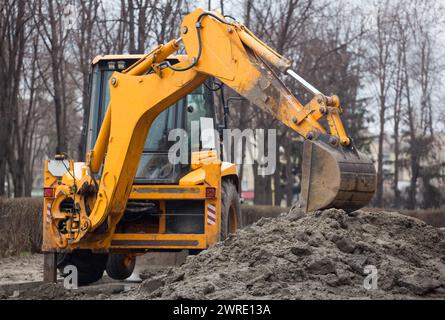 Ein großer gelber Bagger steht in der Mitte der Straße in der Nähe des Grabens. Stockfoto