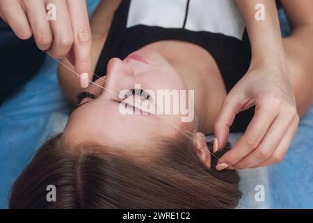 Meister korrigiert Make-up gibt Form und Faden zupft Augenbrauen in einem Schönheitssalon. Professionelle Pflege von Gesicht und Augenbrauen. Stockfoto