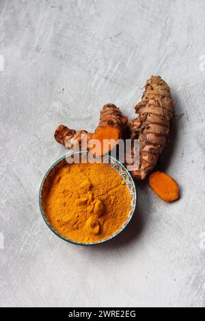 Kurkumapulver in der Schüssel und frische Kurkuma-Wurzel auf strukturiertem Hintergrund mit Platz für Text. Natürliches Antioxidans Nahaufnahme. Stockfoto