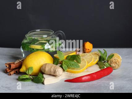 Teekanne aus Glas mit Ingwertee, Zitrone, Kurkuma-Wurzel und Minze auf grauem Hintergrund mit Platz für Text. Kälte- und Grippesaison Konzept. Stockfoto