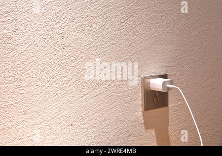 Weißes Mobiltelefon-Ladegerät, das in die Steckdose an der Zimmerwand einschneidet Stockfoto