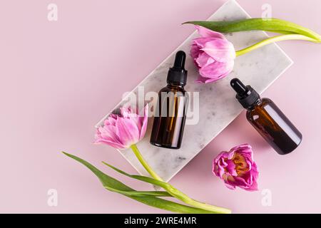 Zwei Kosmetikflaschen mit einer Pipette eines natürlichen Bio-Produkts liegen auf einem Podium aus weißem Marmor mit feinen Tulpen. Leeres Layout. Verpackung Stockfoto