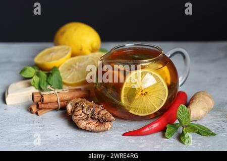 Teekanne aus Glas mit Ingwertee, Zitrone, Kurkuma-Wurzel und Minze auf grauem Hintergrund mit Platz für Text. Kälte- und Grippesaison Konzept. Stockfoto