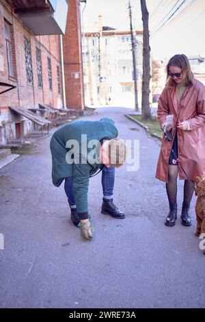 Der Besitzer räumt den Abfall des Hundes auf einem Spaziergang vom Kakapoo Stockfoto