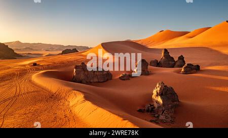 Landschaft des Roten Tadrart in der Sahara, Algerien. Felsformationen zwischen den roten Dünen. Zahlreiche Spuren von Geländewagen Stockfoto