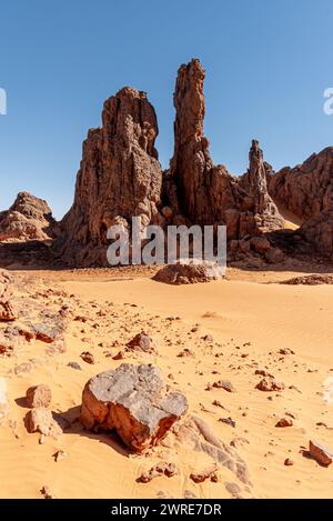 Tadrart-Landschaft in der Sahara, Algerien. Ein Stein, der auf dem Sand vor einer steilen Felsformation liegt Stockfoto