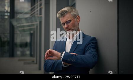 Alter älterer kaukasischer Mann reifer männlicher Arbeitgeber Unternehmer mittleren Alters Geschäftsmann in der Stadt lehnt sich an Wand Bürogebäude an Stockfoto