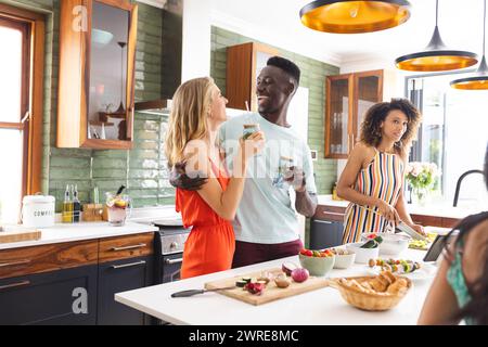 Die junge kaukasische Frau in einem orangen Kleid lacht mit einem jungen Afroamerikaner, der einen Drink hält Stockfoto