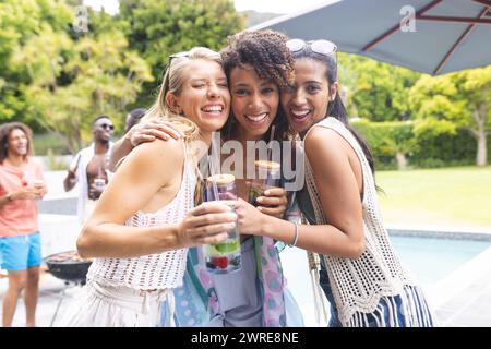 Drei verschiedene weibliche Freundinnen nehmen sich an und lächeln bei einer Poolparty im Freien Stockfoto