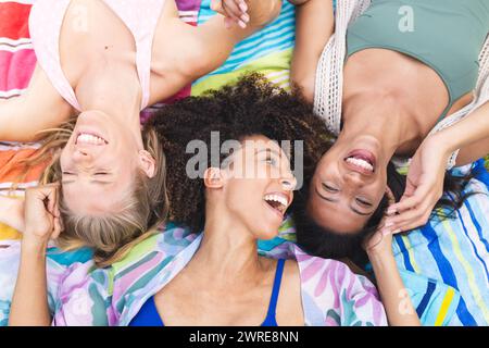 Verschiedene Freundinnen legen sich hin, Köpfe zusammen und lachen fröhlich Stockfoto