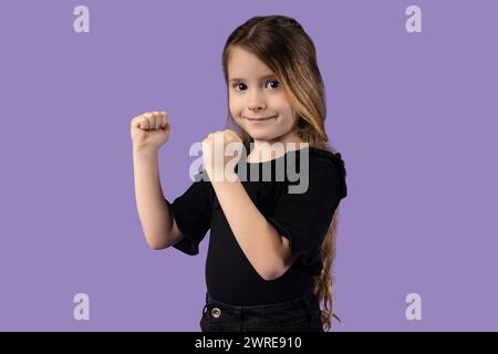 Kleines blondes Mädchen, das ihre Hände in einer Kampfposition auf einem lila Hintergrund hält, das Konzept der Selbstverteidigung der Kinder. Kindersicherheit. Hohe qu Stockfoto