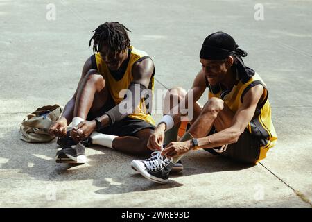 Fröhliche schwarze Männer binden vor dem Streetballspiel Schuhschnürsenkel Stockfoto