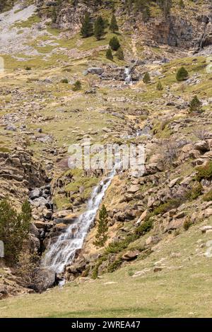 Ruhige Berglandschaft mit einem kaskadierenden Wasserfall, der durch zerklüftetes, felsiges Gelände in kargem Grün fließt Stockfoto