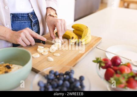 Die kaukasische Frau schneidet Bananen auf einem hölzernen Schneidebrett Stockfoto