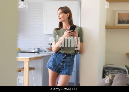 Weiße Frau mit Telefon steht in einer modernen Küche Stockfoto