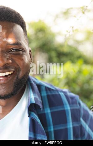 Afroamerikaner mit einem strahlenden Lächeln, trägt ein blaues kariertes Hemd, mit Kopierraum, in einem Garten Stockfoto