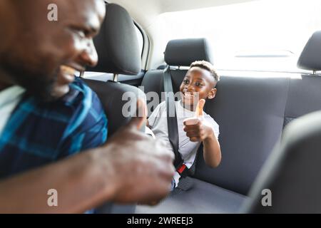 Afroamerikaner Vater und Sohn teilen einen freudigen Moment in einem Auto, beide geben die Daumen hoch Stockfoto