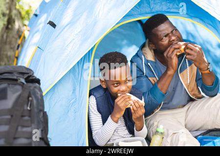 Afroamerikanischer Vater und Sohn genießen Sandwiches beim Camping Stockfoto