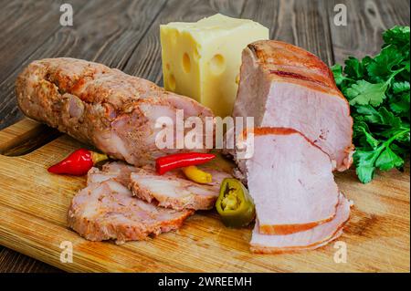 Nahaufnahme einer Reihe hausgemachter Würstchen und geräucherter Fleischsorten mit Käse, Paprika und Petersilie. Stockfoto