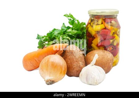 Heiße Paprika in einem Glasgefäß und daneben Kartoffeln, Zwiebeln, Knoblauch und Karotten mit Petersilie. Isolierter Hintergrund Stockfoto