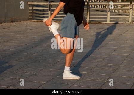 Eine Frau in Sportbekleidung streckt ihr Bein auf dem Bürgersteig Stockfoto