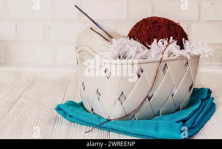 Mehrfarbige Garne, Knäuel und Kugeln aus Wollgarn, Stricknadeln, in einer Box, auf weißem Backsteinhintergrund. Konzept von Stricken, Handarbeit, Handma Stockfoto