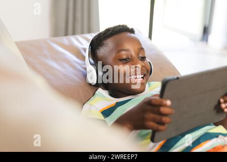 Der afroamerikanische Junge genießt ein Tablet, während er Kopfhörer trägt Stockfoto