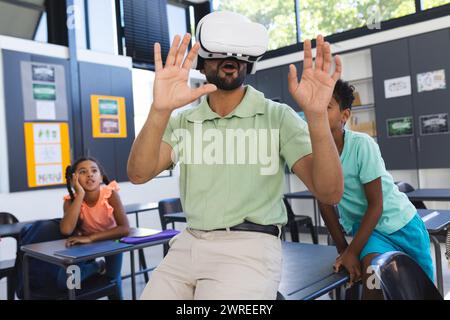 Junger asiatischer Lehrer erlebt virtuelle Realität, mit birassischen Kindern, die in einem Klassenzimmer zuschauen Stockfoto