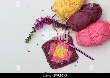 Rosa gehäkelte Granny quadratisch, weiche Baumwoll-Garnbällchen in verschiedenen rosa Farbtönen. Weißer Hintergrund mit Kopierraum. Frühlingshäkelkonzept. Stockfoto