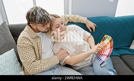 Ein Mann und eine Frau entspannen sich auf einer Couch im Wohnzimmer und untersuchen gemeinsam Farbmuster, symbolisieren Wahlmöglichkeiten und Verbesserungen. Stockfoto