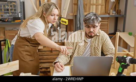 Eine Frau und ein Mann in einer Werkstatt arbeiten an einem Laptop zusammen, umgeben von Holzwerkzeugen. Stockfoto