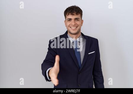 Junger hispanischer Geschäftsmann mit Anzug und Krawatte lächelnd und freundlich, der Handschlag als Begrüßung und Begrüßung anbietet. Erfolgreiches Geschäft. Stockfoto