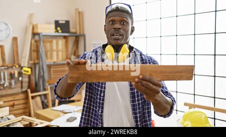 Der afroamerikanische Zimmermann untersucht Holz in einer gut beleuchteten Werkstatt mit Sicherheitsausrüstung. Stockfoto