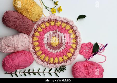 Foto von oben mit Baumwoll-Garnbällchen, Häkelnadel und Blumen. Handgefertigtes Dekoelement. Stockfoto