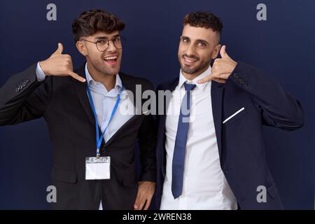 Zwei hispanische Geschäftsmänner, die Geschäftskleidung tragen, lächeln und mit Hand und Fingern telefonieren. Kommunizierende Konz Stockfoto