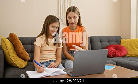 Mutter und Tochter können sich in einem gemütlichen Wohnzimmer mit einem Laptop austauschen, was Familie, Lernen und eine entspannte Atmosphäre zu Hause widerspiegelt. Stockfoto