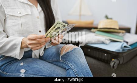 Eine junge hispanische Frau zählt uns Dollar, bevor sie mit einem Koffer drinnen sitzt. Stockfoto