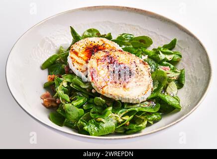Gegrillter Ziegenkäse auf einem Bett mit frischem Spinatsalat in einer Keramikschale, die vegetarische Gourmetküche eingefangen Stockfoto