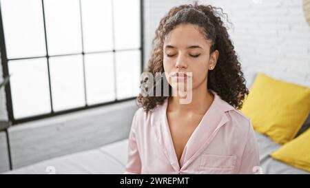 Zu Hause Zen, schöne junge hispanische Frau, die auf dem Bett sitzt und sich auf morgendliches Yoga konzentriert, um Balance und Entspannung im Schlafzimmer zu finden Stockfoto