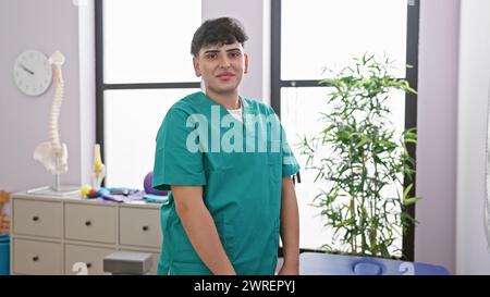 Ein junger Mann in Peelings steht zuversichtlich drinnen in einer Rehabilitationsklinik, mit medizinischen Geräten und Pflanzen im Hintergrund. Stockfoto