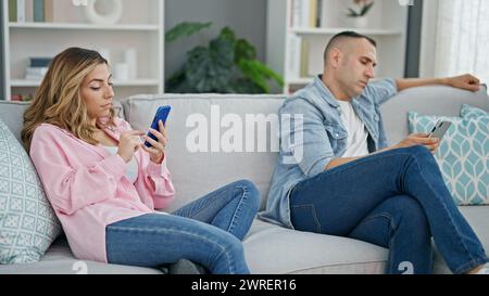 Mann und Frau, die zu Hause auf dem Sofa sitzen und Smartphones benutzen Stockfoto